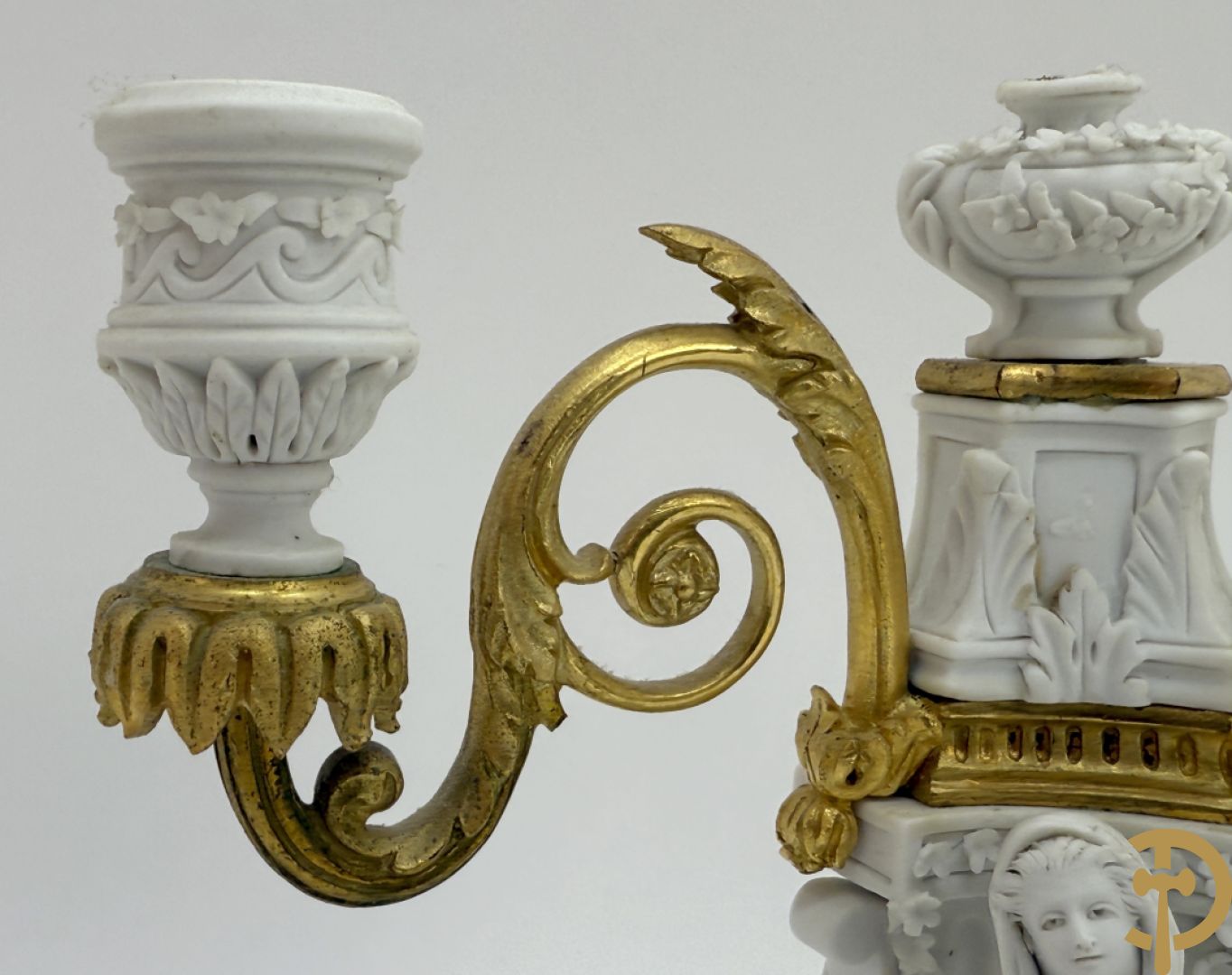 Driedelige porseleinen garnituur met bronsbeslag bestaande uit pendule met dame en amfoor geflankeerd door paar kandelaars bezet met personages