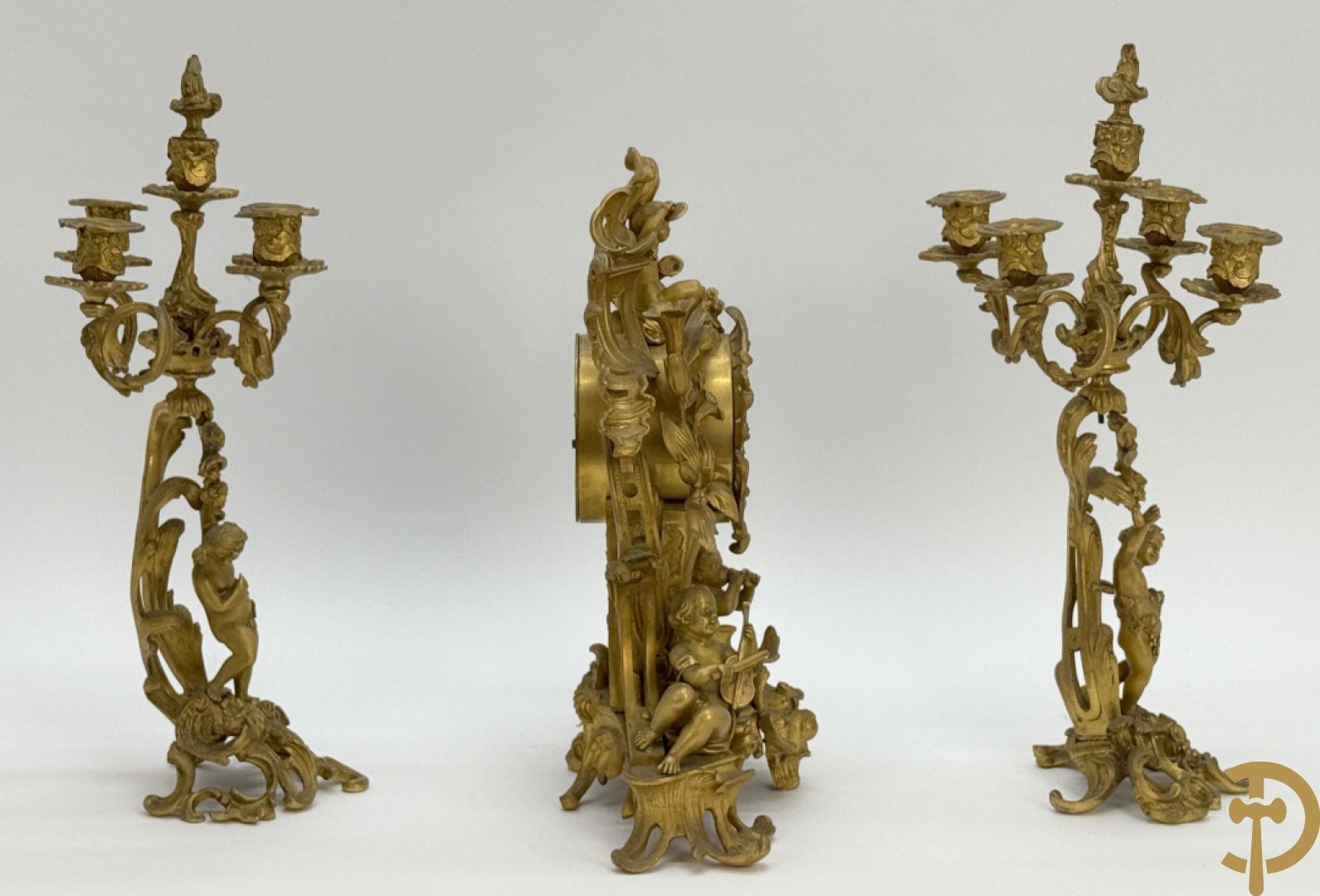 Driedelige vuurvergulde bronzen garnituur, Louis XV stijl, bestaande uit middenstuk met klok omgeven door musicerende cupido