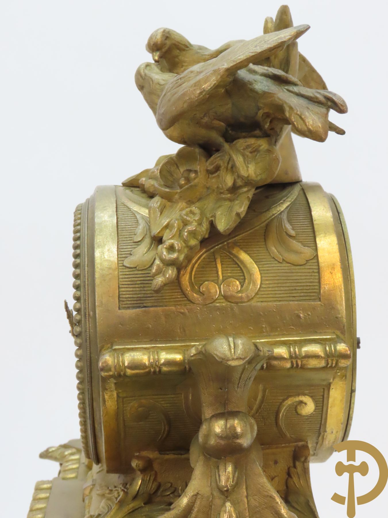 Vergulde pendule in zamak, wijzerplaat bezet met porseleinen plakkettes - bovenaan met vogelpaar, zijdelings met kariathyden houdende een bloementroffee - onder glazen stolp