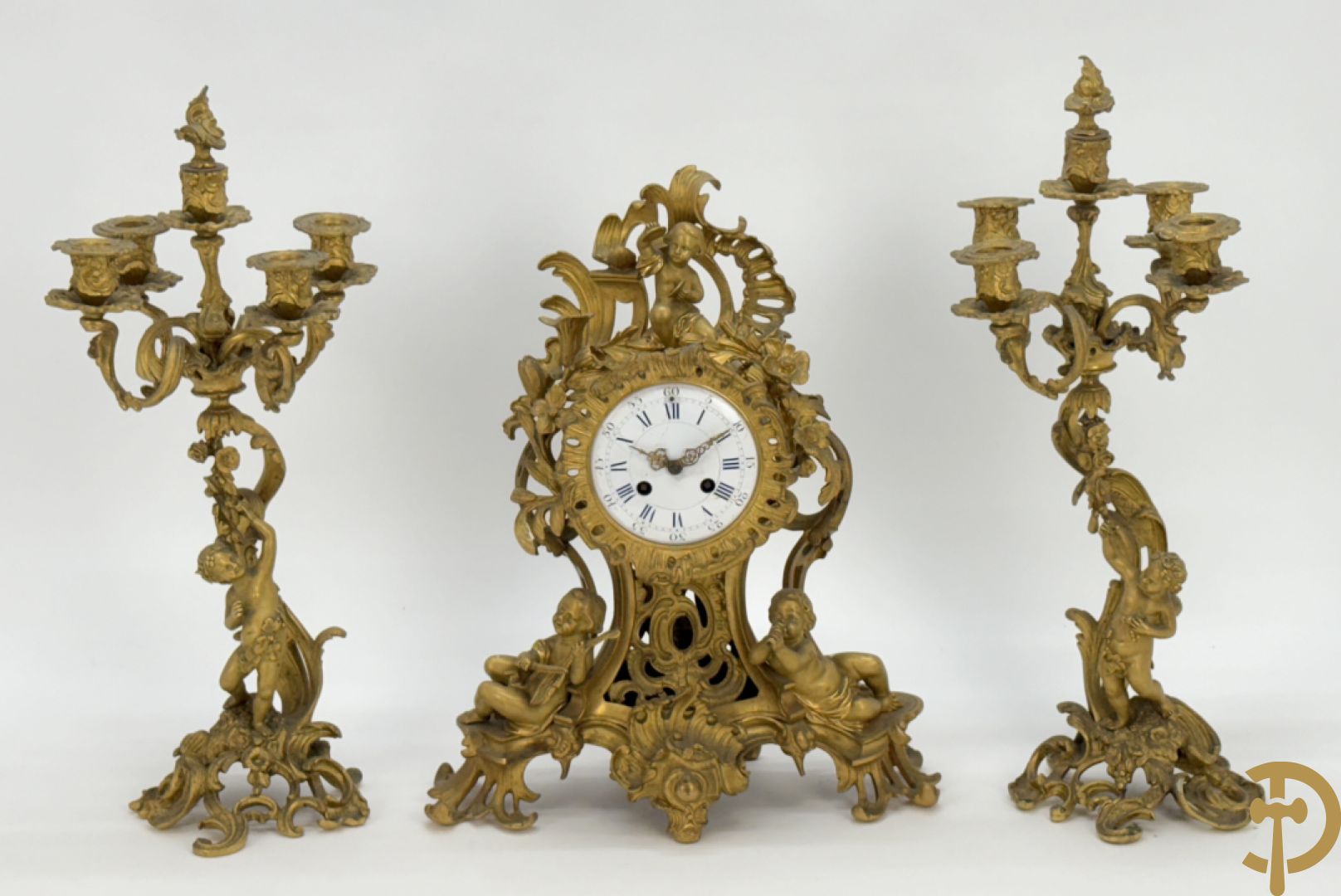 Driedelige vuurvergulde bronzen garnituur, Louis XV stijl, bestaande uit middenstuk met klok omgeven door musicerende cupido