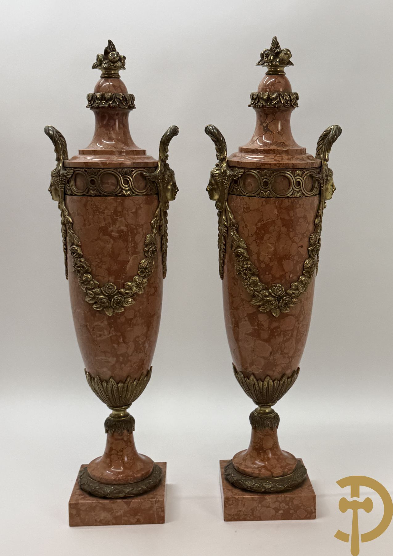 Paar oranje/rode marmeren cassolettes, zijdelings bezet met dameshoofden dragende een guirlande van bloemen - bovenaan met bloementroffee