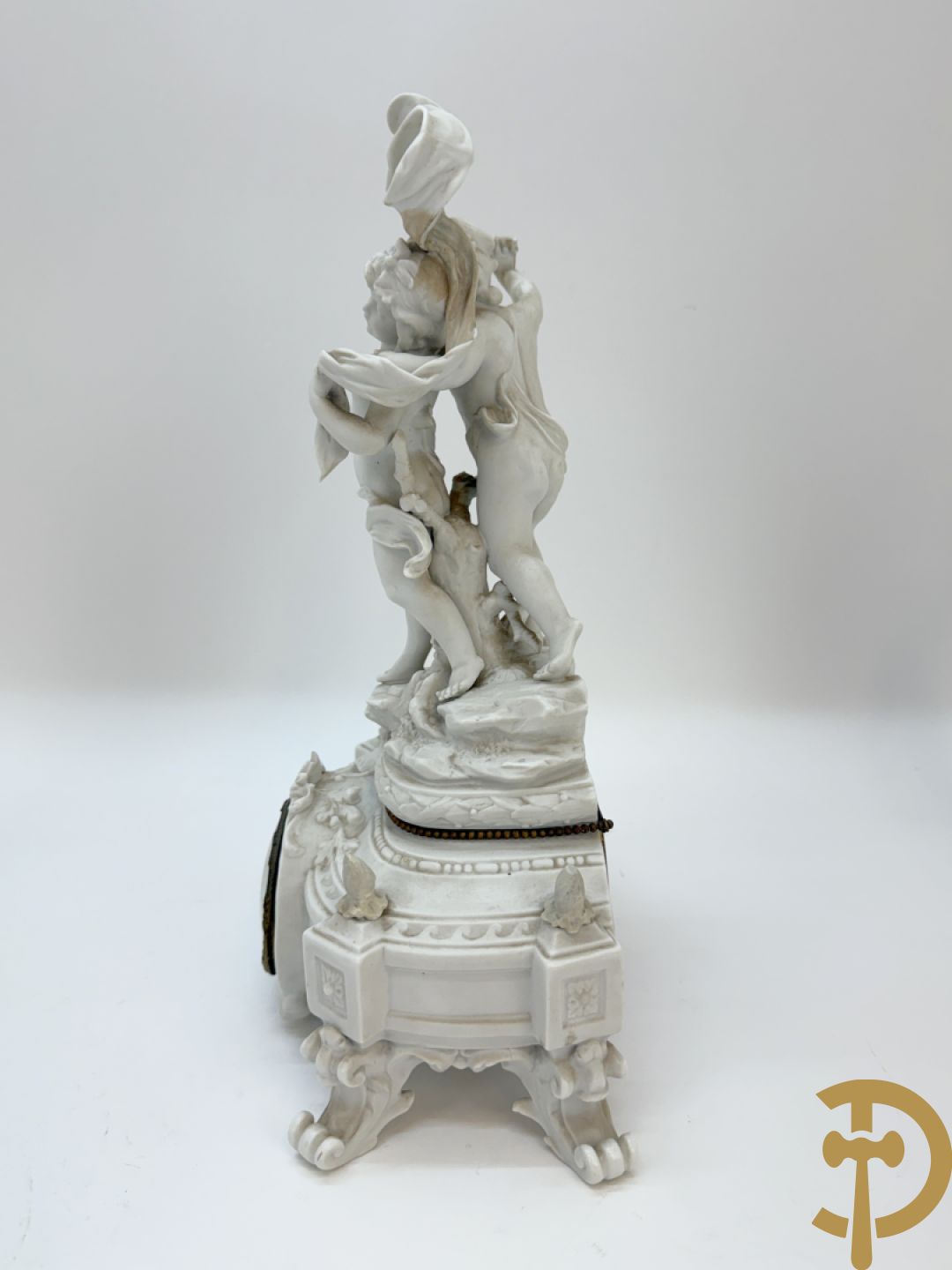 Driedelige porseleinen garnituur bestaande uit pendule bezet met lieftallig koppel, geflankeerd door paar kandelaars met cupido