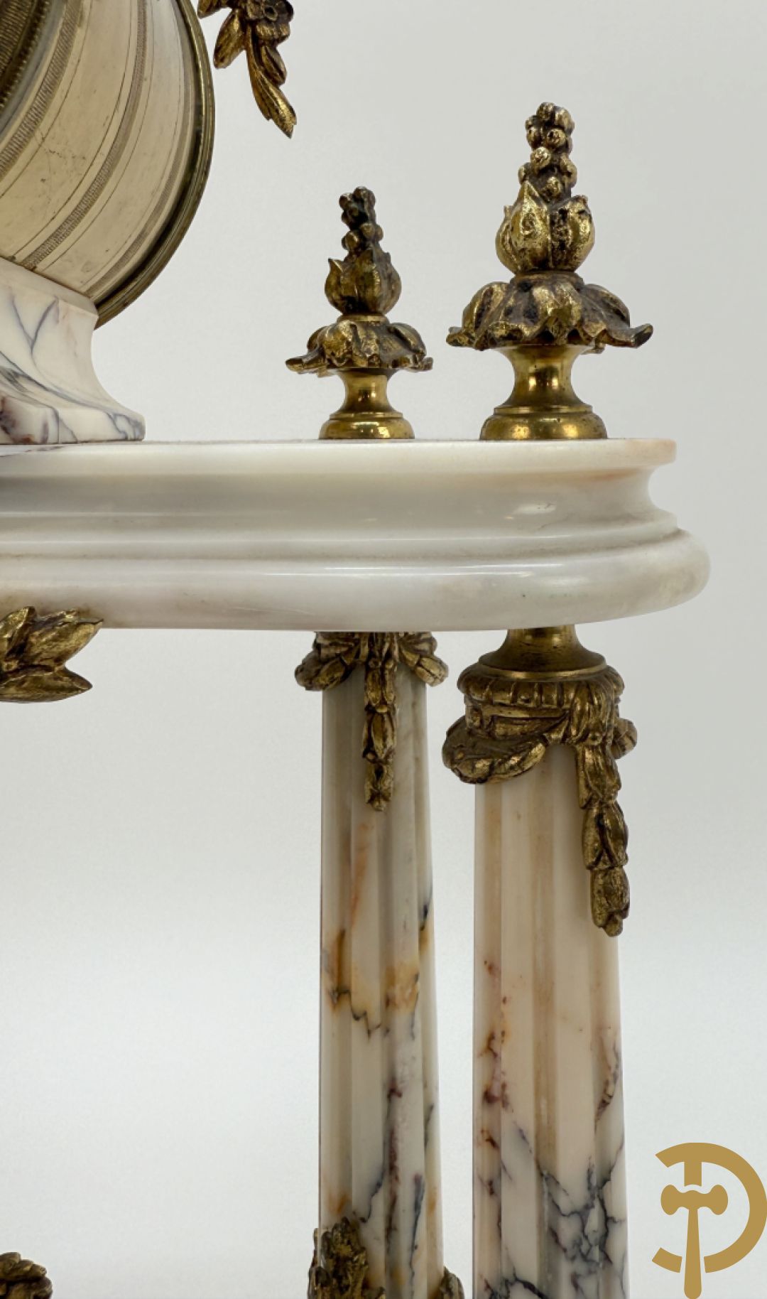 Driedelige wit marmeren garnituur bestaande uit vierzuilenpendule met bloemen en troffee geflankeerd door paar cassolettes met ramskoppen bezet