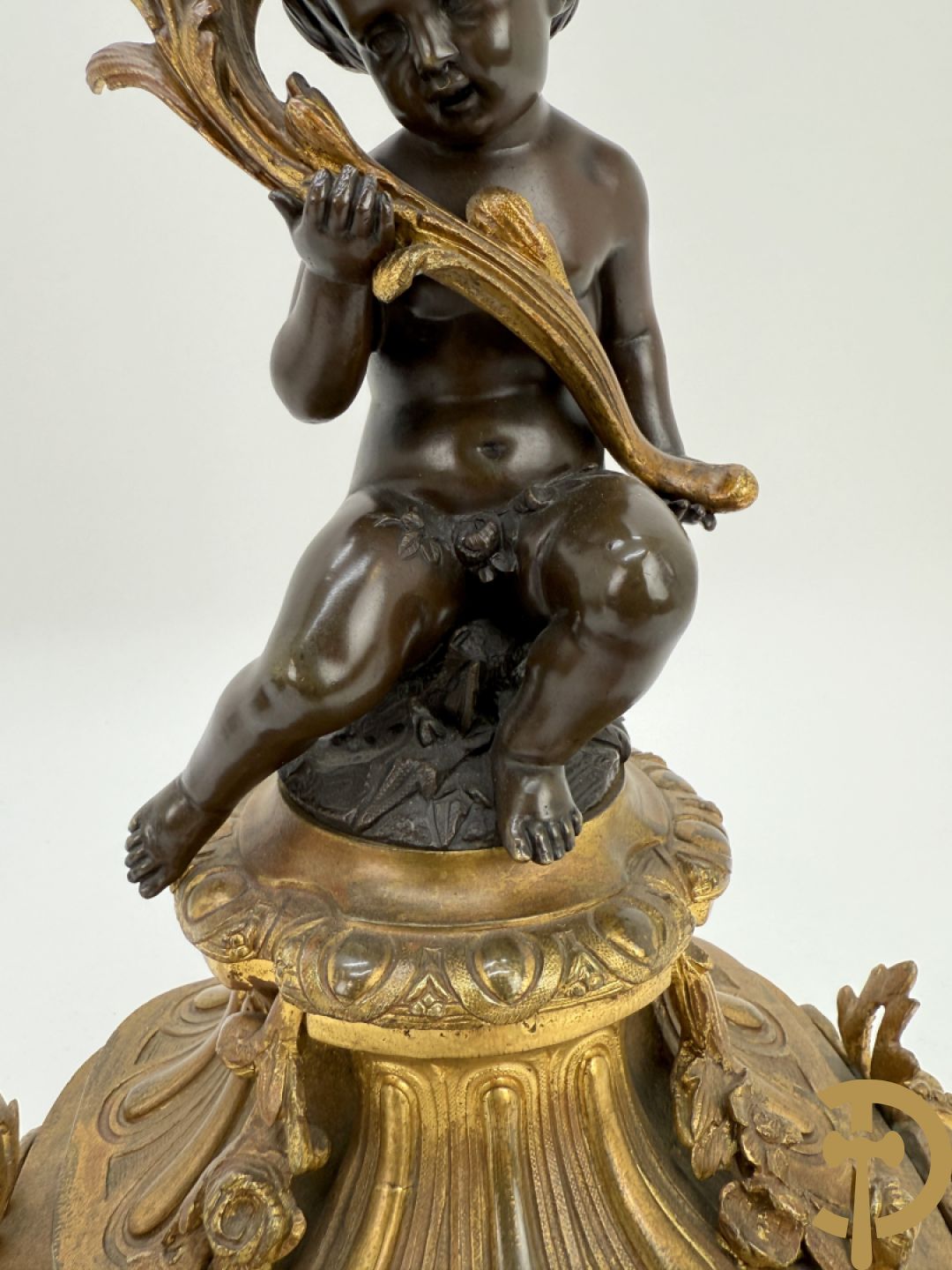 Driedelige bronzen garnituur bestaande uit middenstuk met bronzen vuurvergulde klok, Daubrée gemerkt à Nancy, bovenaan bekroond met Cleopatra met drinkbeker - getekend van Cumberworth sculpteur - geflankeerd door paar cupido