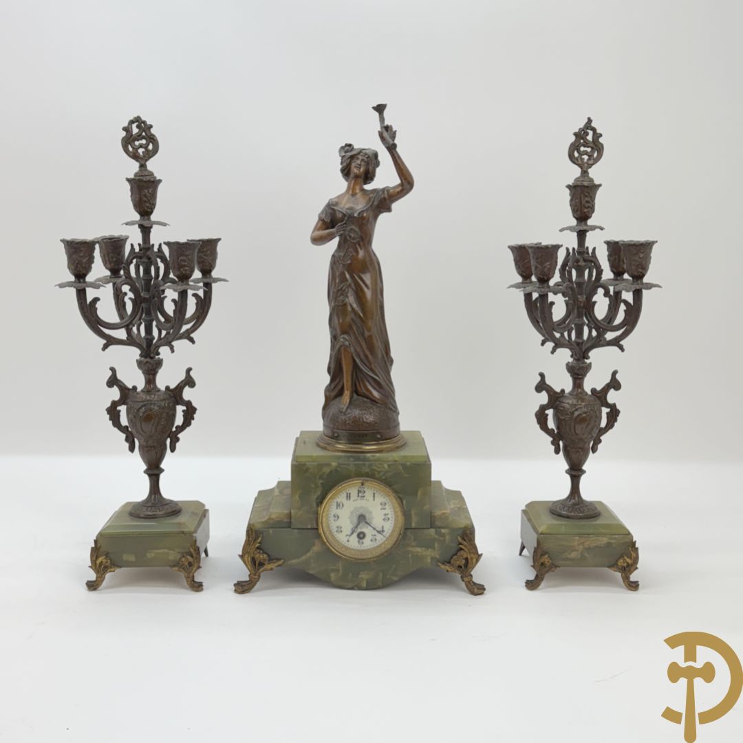 Driedelige zamak garnituur met dame Pavot met bloemen op uurwerk, Rucho getekend, geflankeerd door paar kandelaars