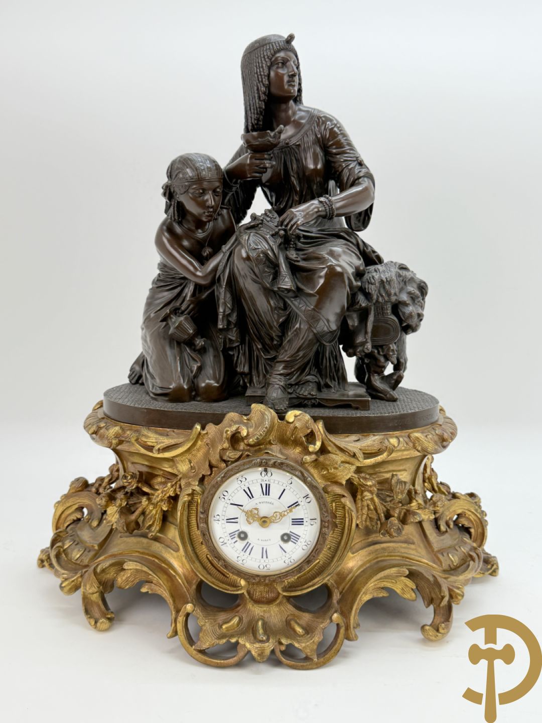 Driedelige bronzen garnituur bestaande uit middenstuk met bronzen vuurvergulde klok, Daubrée gemerkt à Nancy, bovenaan bekroond met Cleopatra met drinkbeker - getekend van Cumberworth sculpteur - geflankeerd door paar cupido