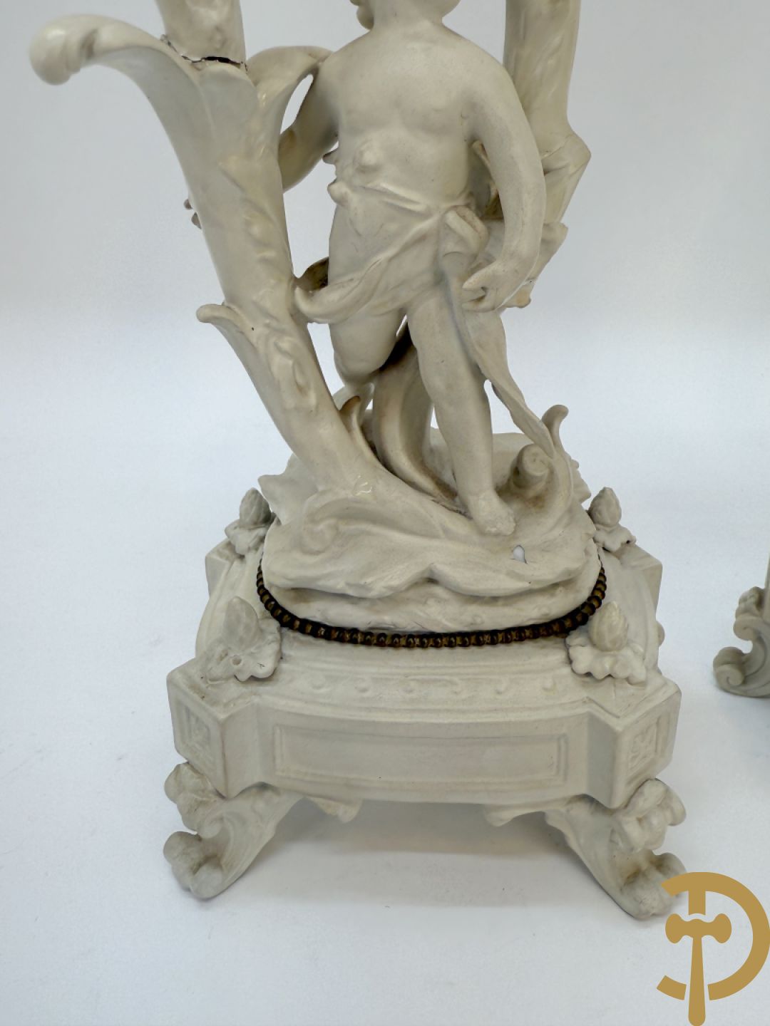 Driedelige porseleinen garnituur bestaande uit pendule bezet met lieftallig koppel, geflankeerd door paar kandelaars met cupido