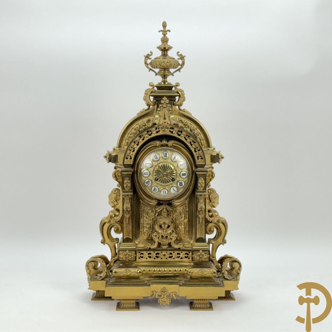 Vuurvergulde bronzen pendule, zijdelings bezet met gevleugelde dames, bovenaan met amfoor