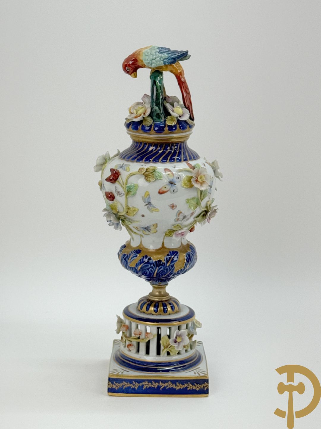 Porseleinen siervaas met handbeschilderd geanimeerd decor bezet met basrelief van bloemen en bovenaan bekroond met deksel met vogel