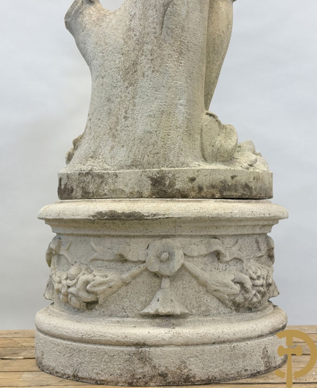 Stenen tuinbeeld van jongeman met mand in de hand op sokkel met guirlandes