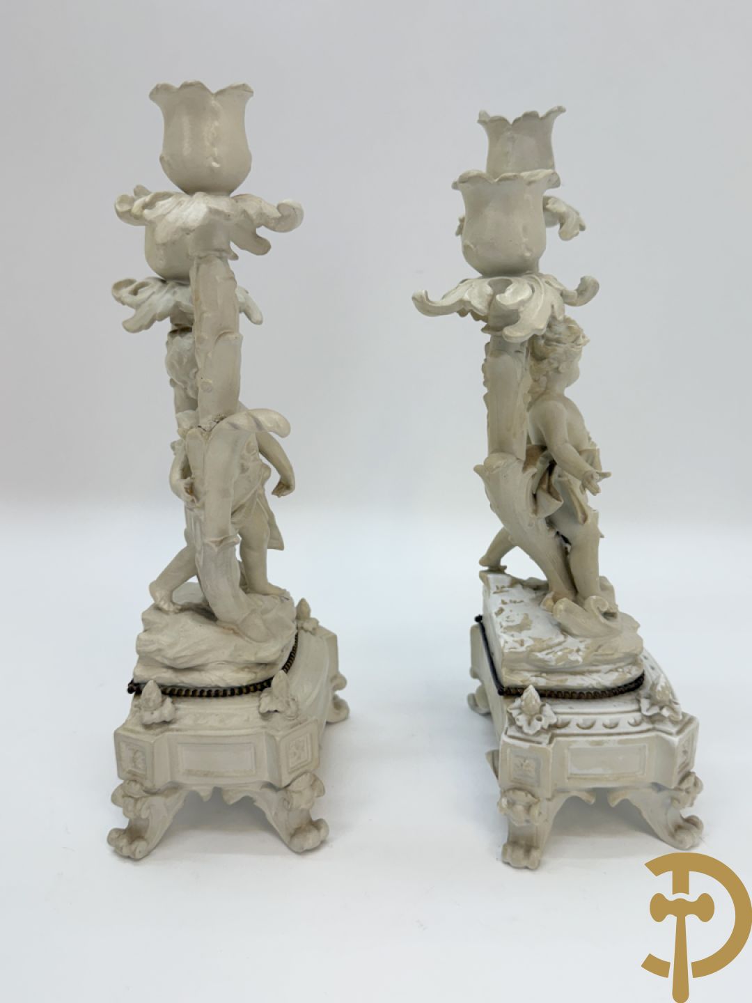 Driedelige porseleinen garnituur bestaande uit pendule bezet met lieftallig koppel, geflankeerd door paar kandelaars met cupido