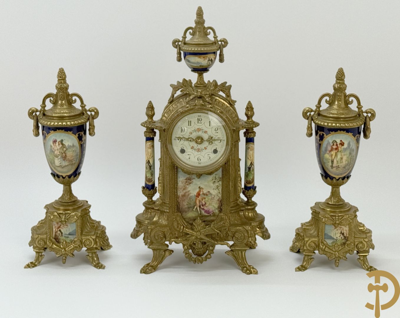 Driedelige koperen garnituur bestaande uit pendule met beschilderd romantisch tafereel en amfoor, zijdelings bezet met paar cassolettes met geanimeerde scènes, onleesbaar getekend rechts onder klok