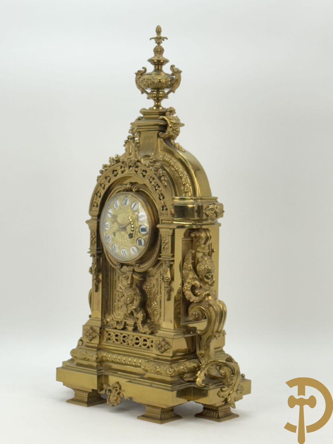 Vuurvergulde bronzen pendule, zijdelings bezet met gevleugelde dames, bovenaan met amfoor