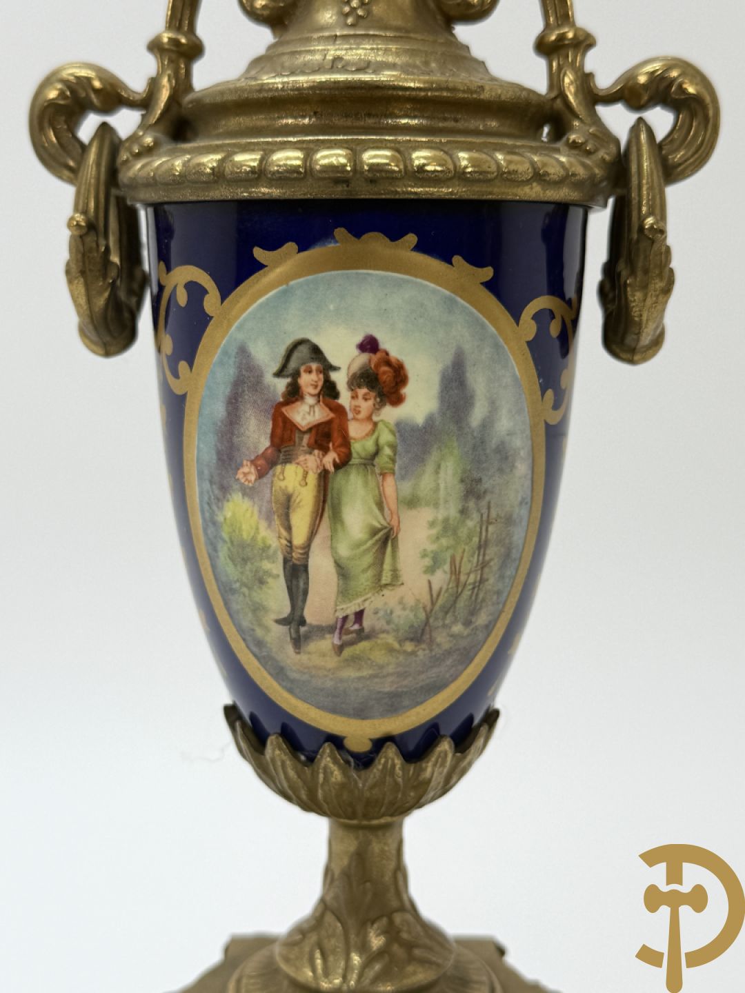 Driedelige koperen garnituur bestaande uit pendule met beschilderd romantisch tafereel en amfoor, zijdelings bezet met paar cassolettes met geanimeerde scènes, onleesbaar getekend rechts onder klok