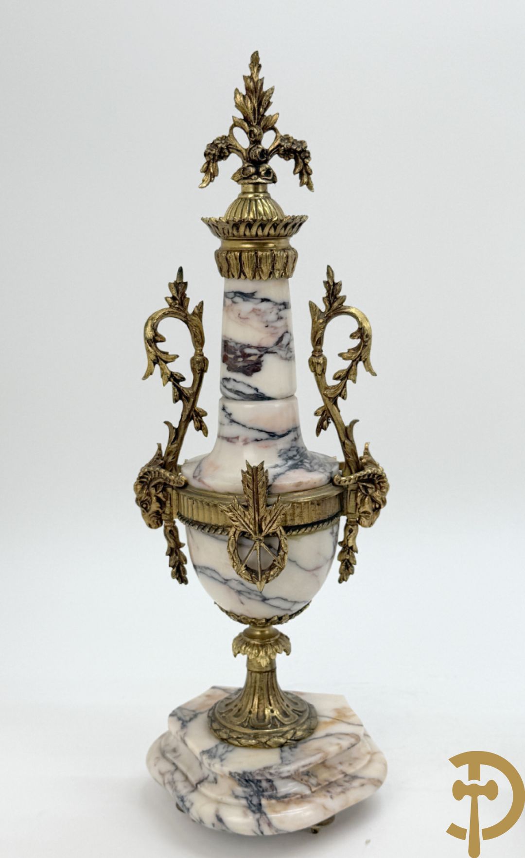 Driedelige wit marmeren garnituur bestaande uit vierzuilenpendule met bloemen en troffee geflankeerd door paar cassolettes met ramskoppen bezet