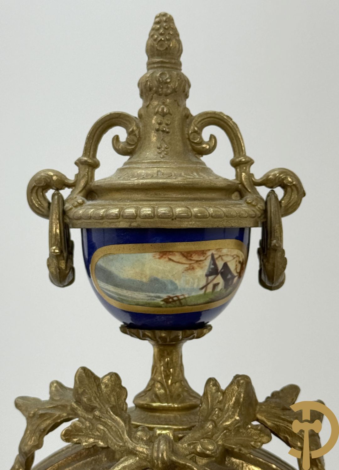 Driedelige koperen garnituur bestaande uit pendule met beschilderd romantisch tafereel en amfoor, zijdelings bezet met paar cassolettes met geanimeerde scènes, onleesbaar getekend rechts onder klok