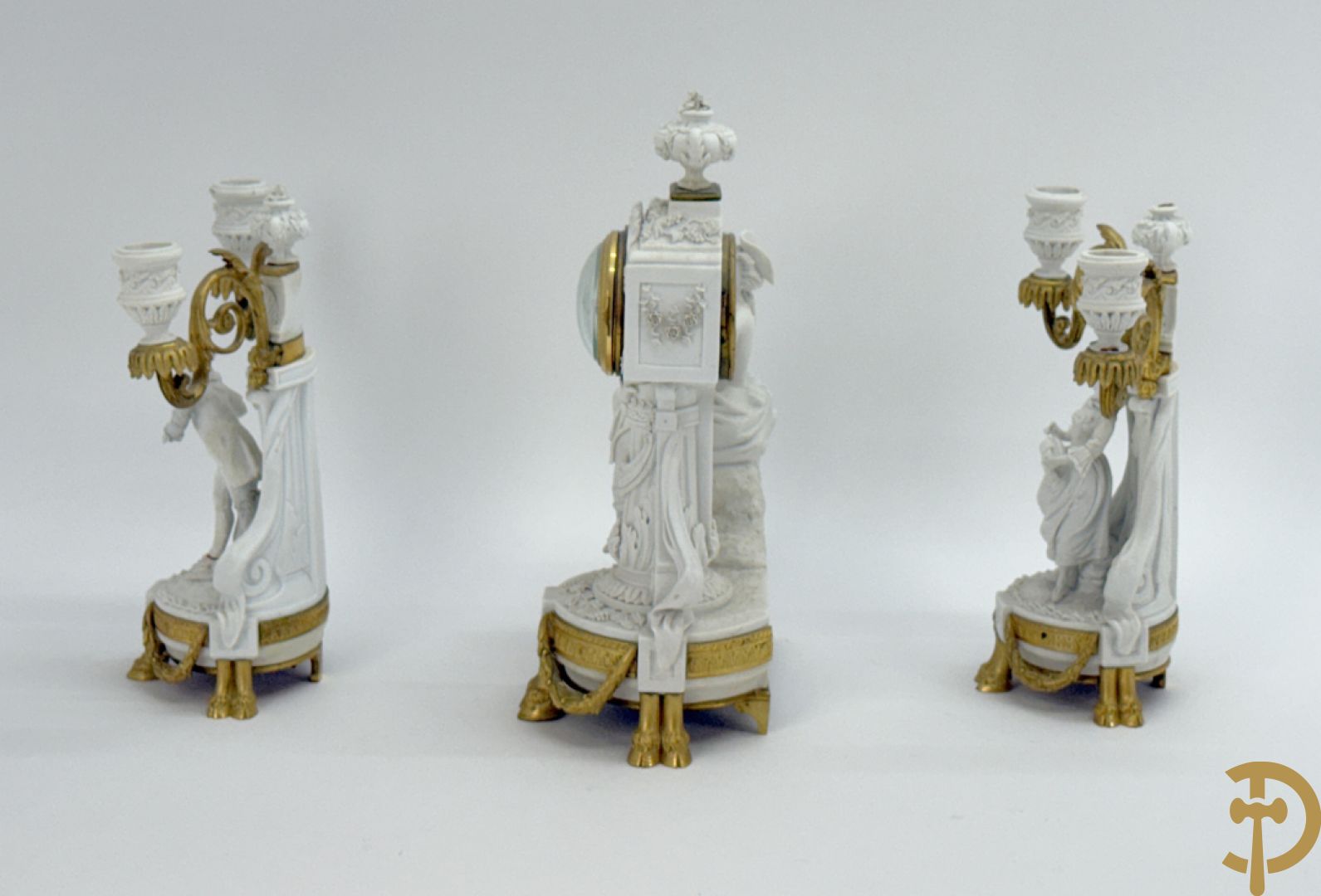 Driedelige porseleinen garnituur met bronsbeslag bestaande uit pendule met dame en amfoor geflankeerd door paar kandelaars bezet met personages
