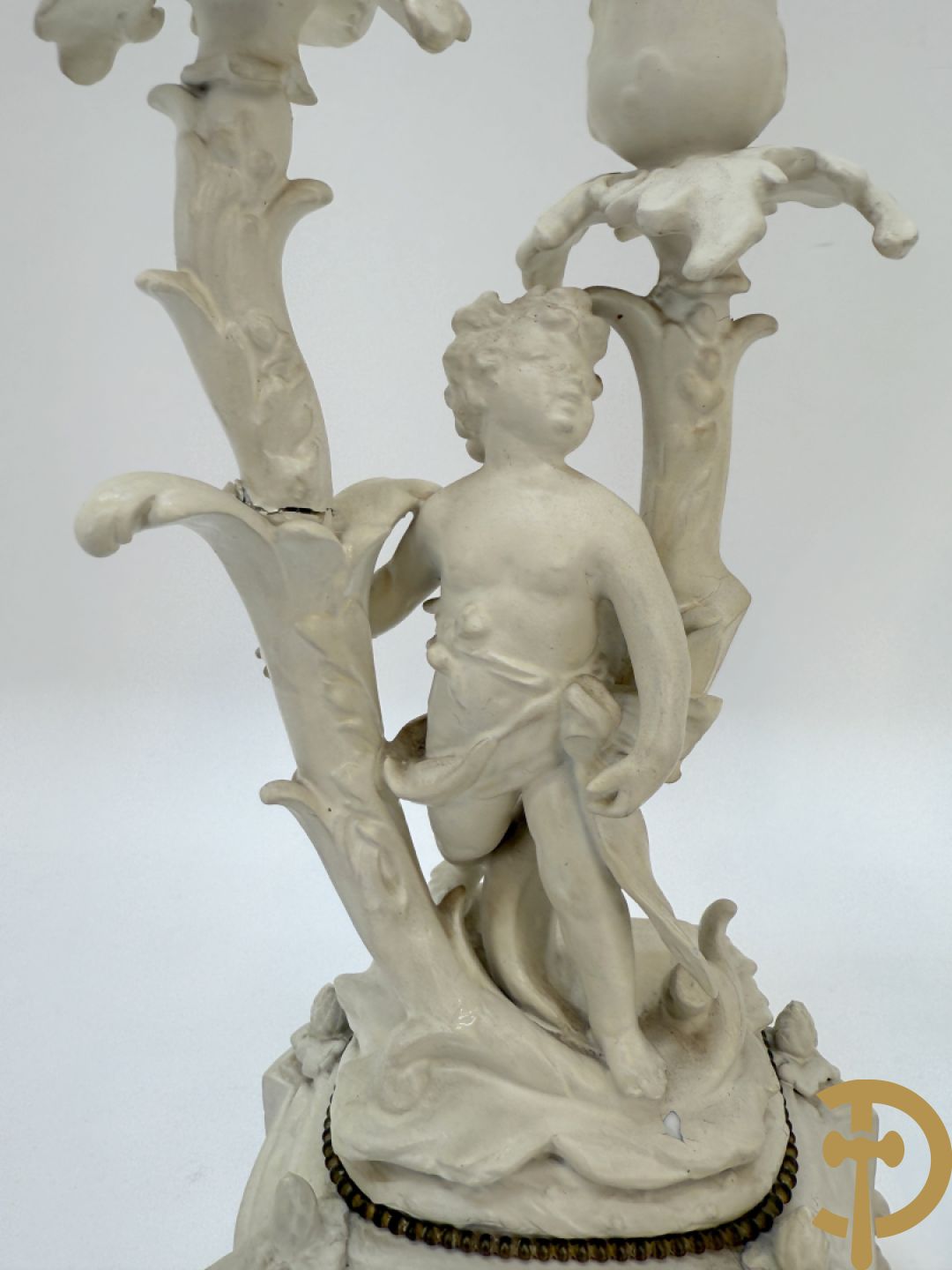 Driedelige porseleinen garnituur bestaande uit pendule bezet met lieftallig koppel, geflankeerd door paar kandelaars met cupido