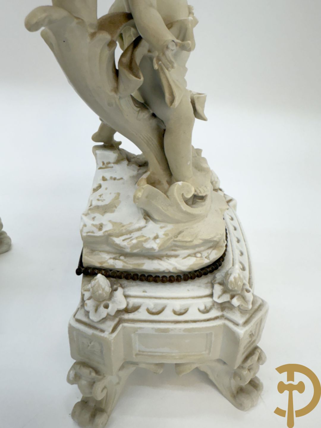 Driedelige porseleinen garnituur bestaande uit pendule bezet met lieftallig koppel, geflankeerd door paar kandelaars met cupido