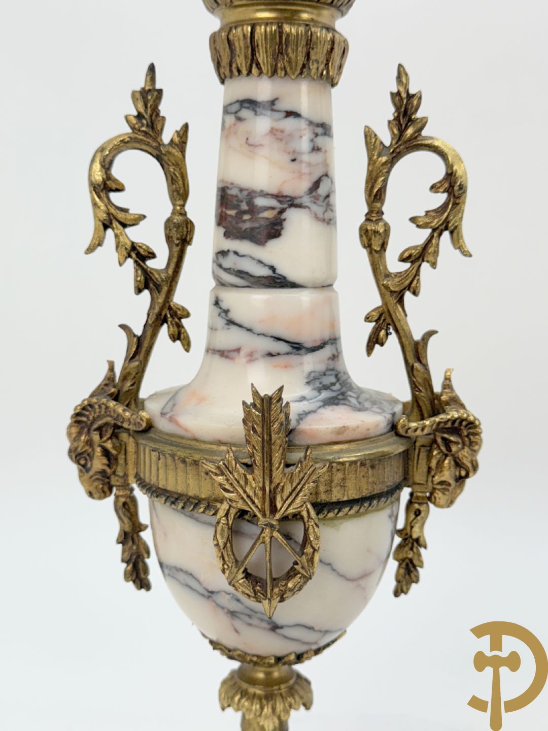 Driedelige wit marmeren garnituur bestaande uit vierzuilenpendule met bloemen en troffee geflankeerd door paar cassolettes met ramskoppen bezet