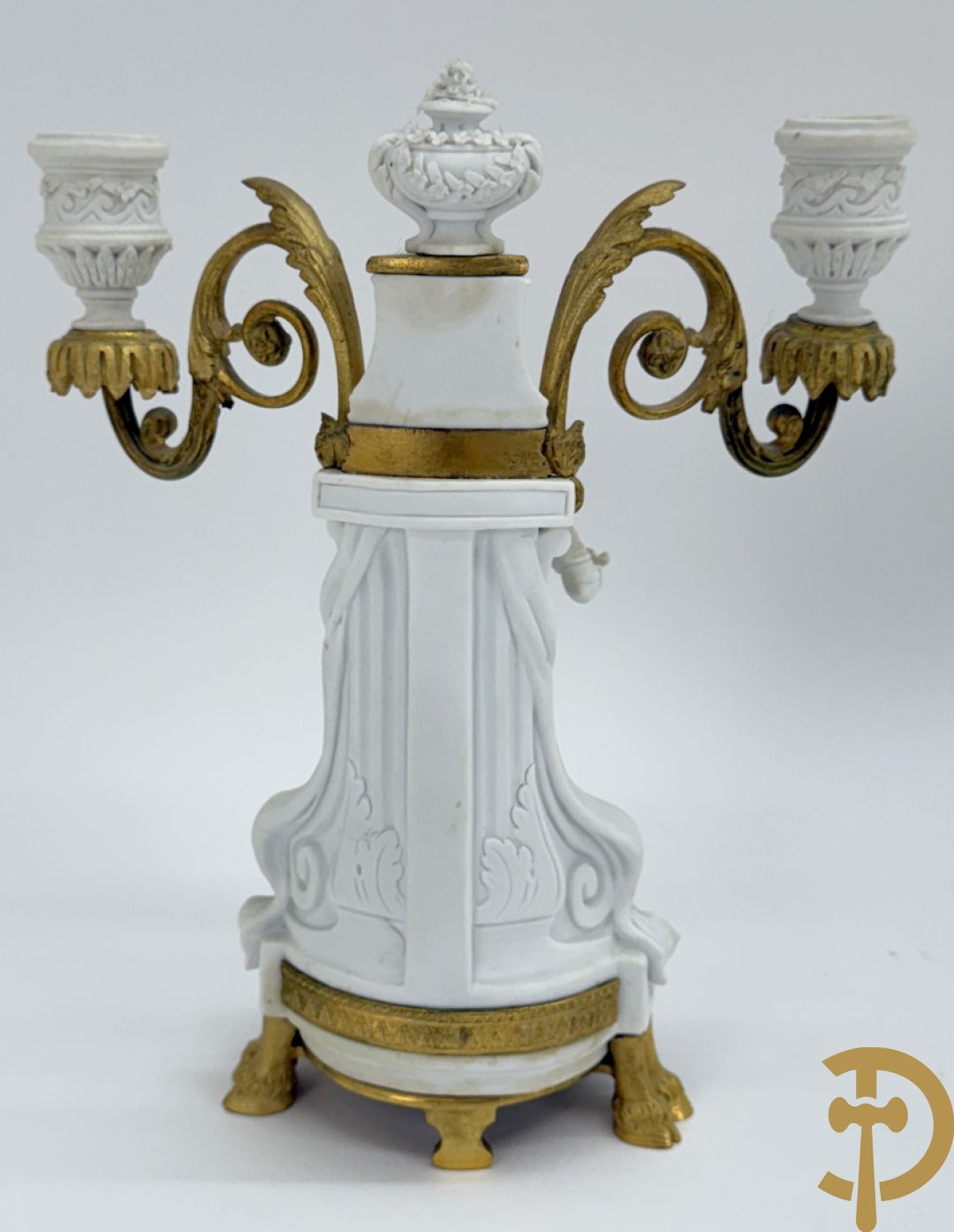 Driedelige porseleinen garnituur met bronsbeslag bestaande uit pendule met dame en amfoor geflankeerd door paar kandelaars bezet met personages