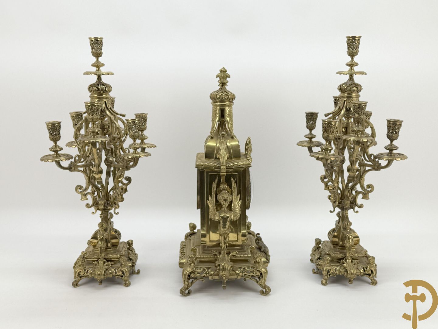Driedelige bronzen vergulde garntiuur bestaande uit klok met medusahoofden en sfinxen, geflankeerd door paar zevenarmige kandelaars met accanthusranken en sfinxen