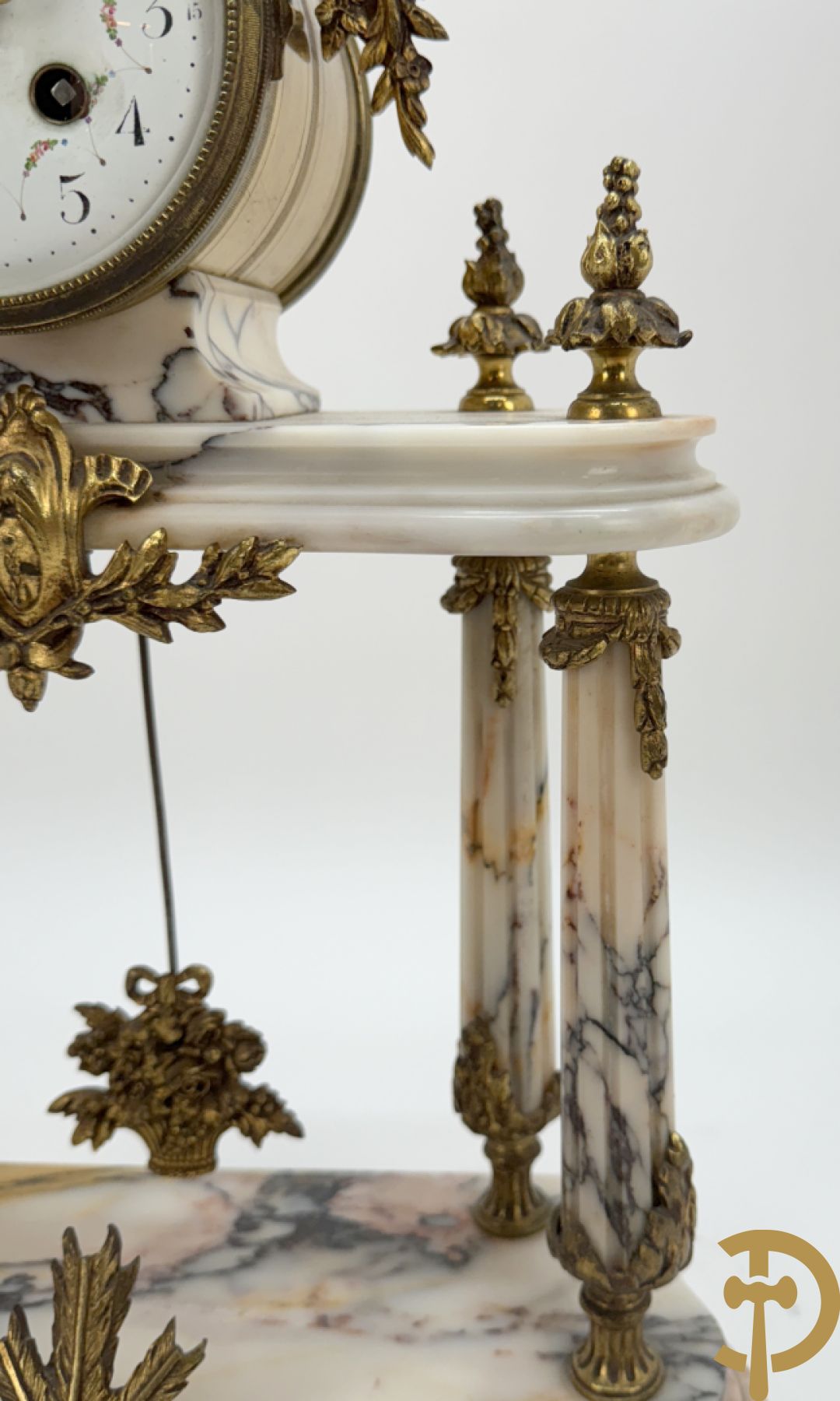 Driedelige wit marmeren garnituur bestaande uit vierzuilenpendule met bloemen en troffee geflankeerd door paar cassolettes met ramskoppen bezet