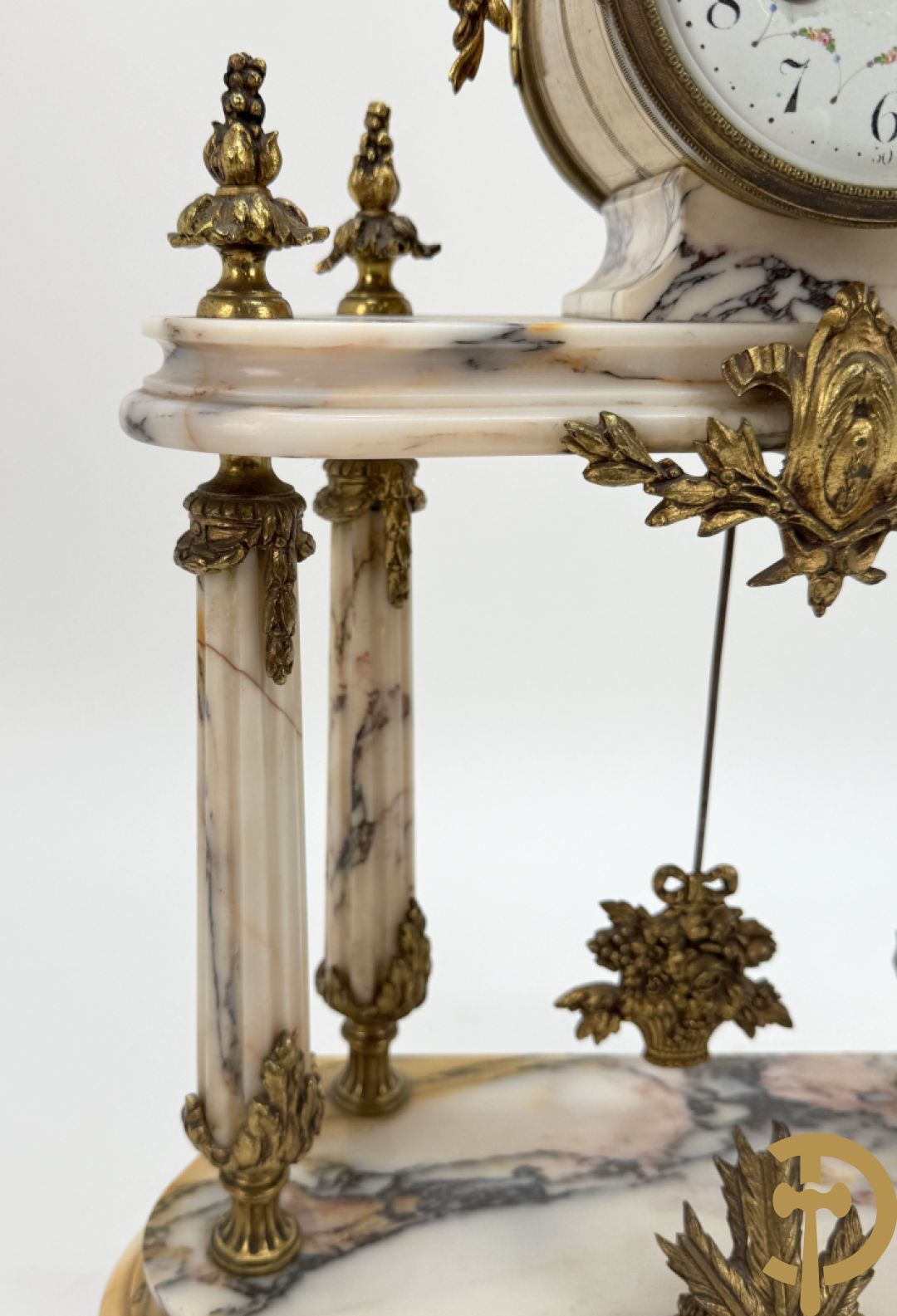 Driedelige wit marmeren garnituur bestaande uit vierzuilenpendule met bloemen en troffee geflankeerd door paar cassolettes met ramskoppen bezet