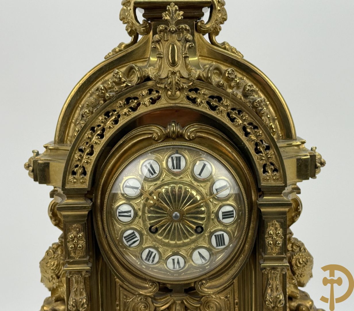 Vuurvergulde bronzen pendule, zijdelings bezet met gevleugelde dames, bovenaan met amfoor