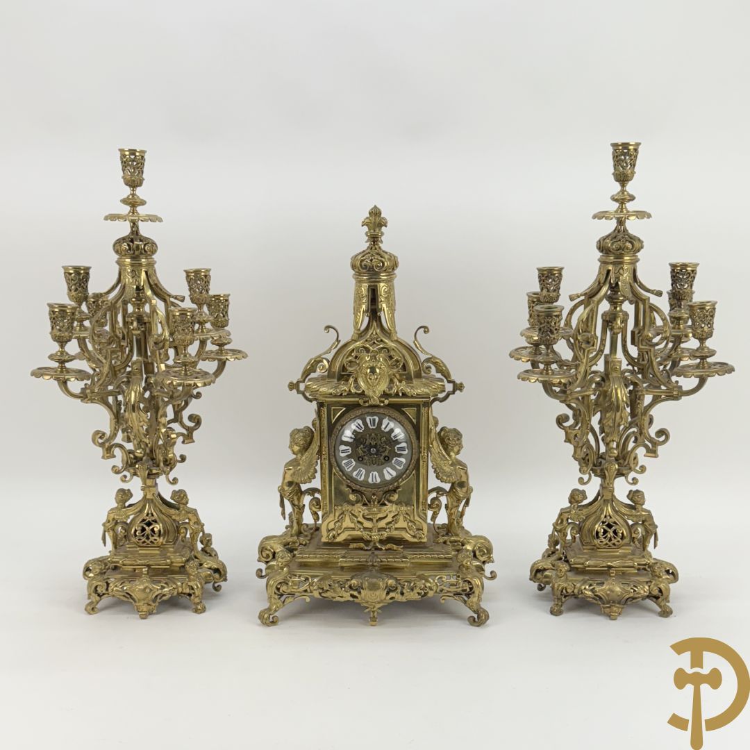 Driedelige bronzen vergulde garntiuur bestaande uit klok met medusahoofden en sfinxen, geflankeerd door paar zevenarmige kandelaars met accanthusranken en sfinxen