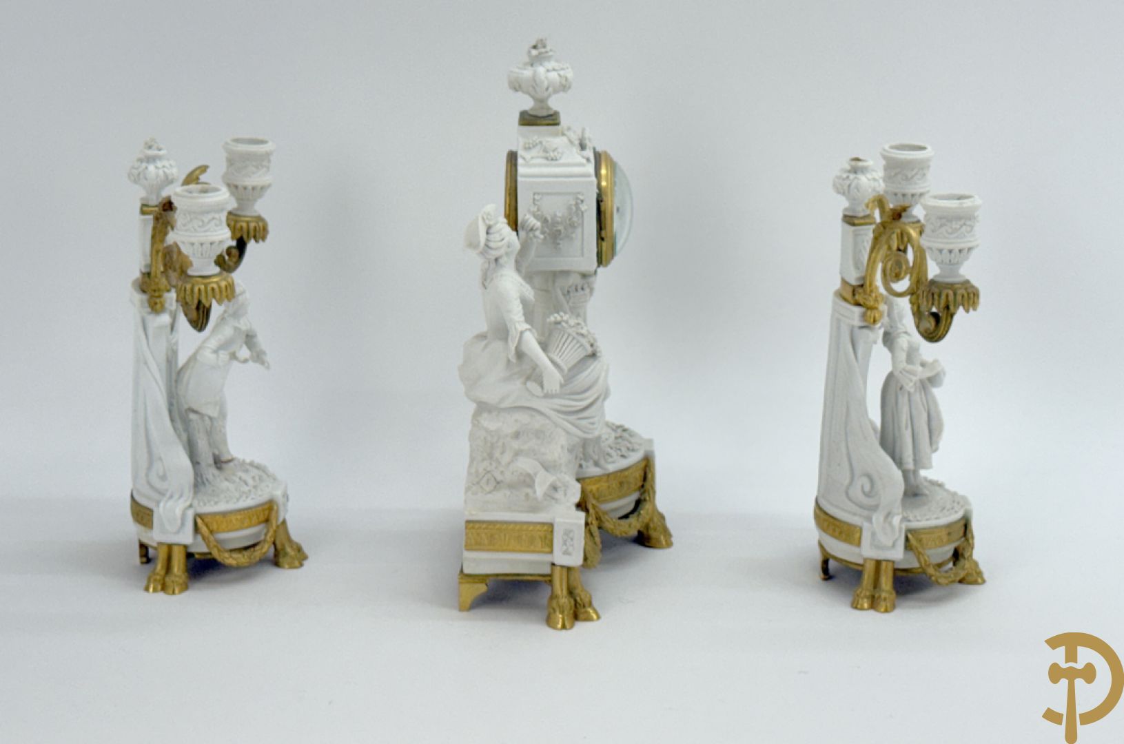 Driedelige porseleinen garnituur met bronsbeslag bestaande uit pendule met dame en amfoor geflankeerd door paar kandelaars bezet met personages