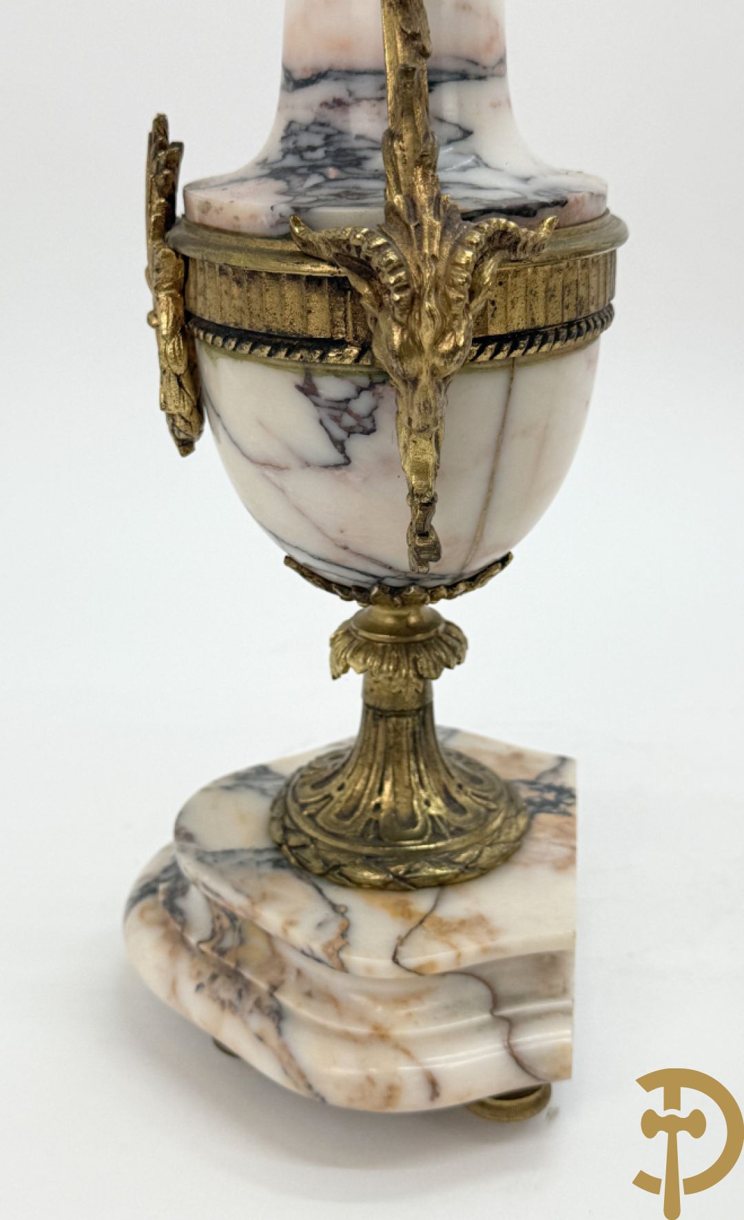 Driedelige wit marmeren garnituur bestaande uit vierzuilenpendule met bloemen en troffee geflankeerd door paar cassolettes met ramskoppen bezet