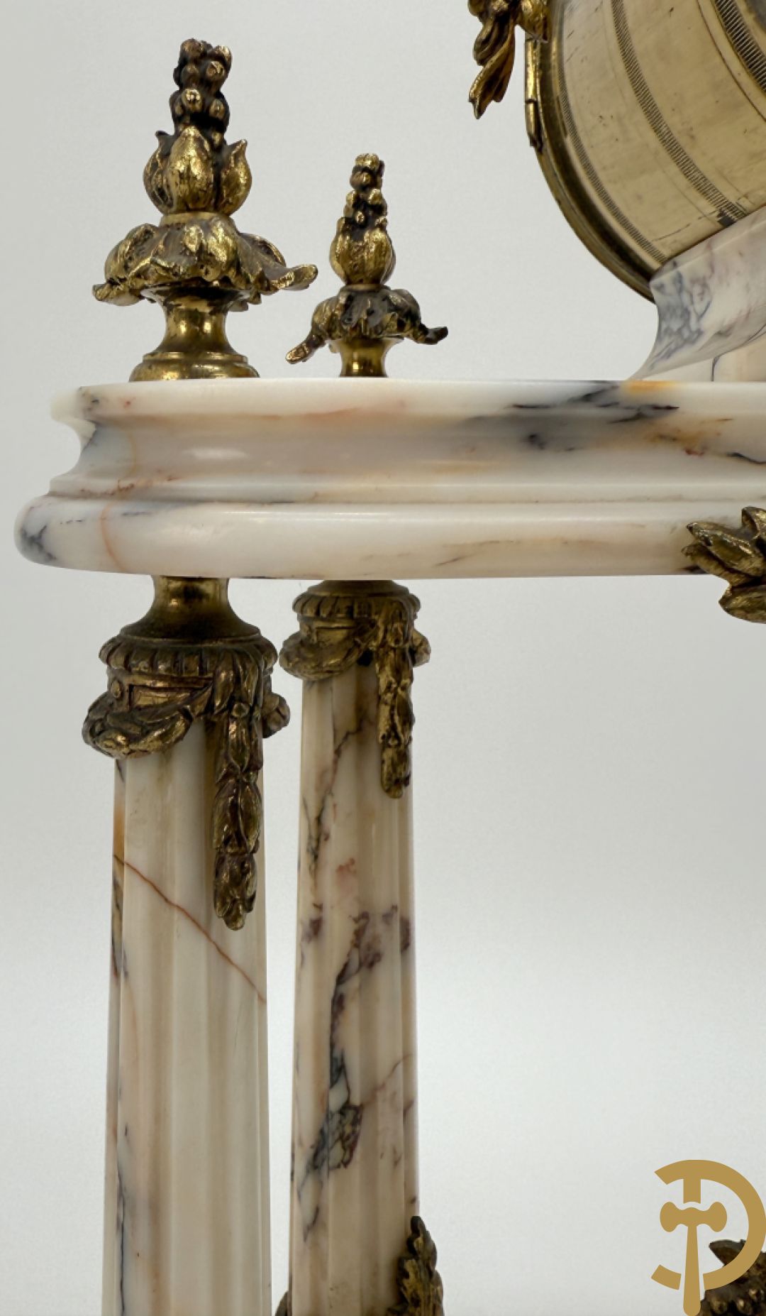 Driedelige wit marmeren garnituur bestaande uit vierzuilenpendule met bloemen en troffee geflankeerd door paar cassolettes met ramskoppen bezet