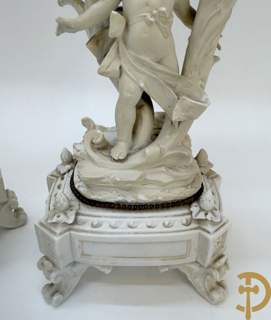 Driedelige porseleinen garnituur bestaande uit pendule bezet met lieftallig koppel, geflankeerd door paar kandelaars met cupido