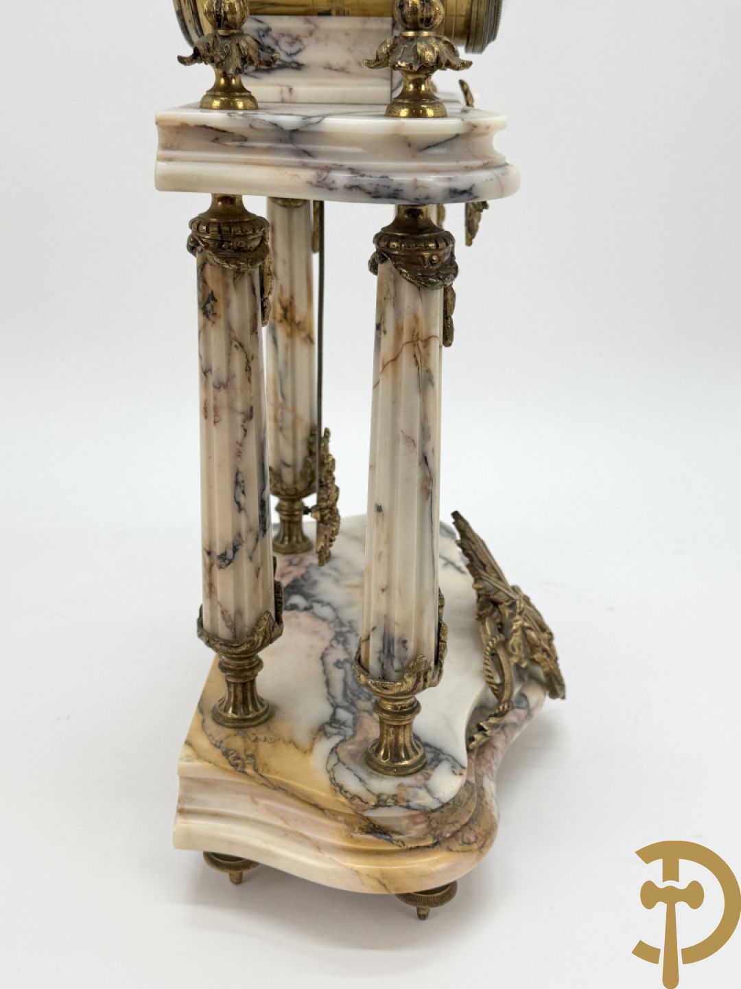 Driedelige wit marmeren garnituur bestaande uit vierzuilenpendule met bloemen en troffee geflankeerd door paar cassolettes met ramskoppen bezet