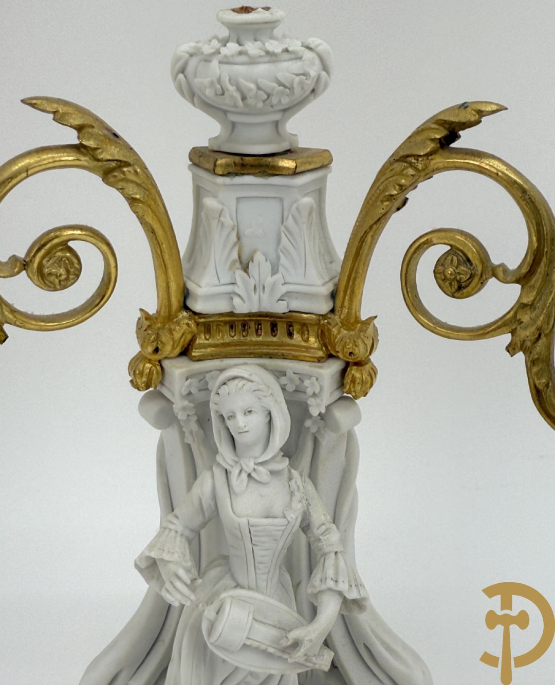 Driedelige porseleinen garnituur met bronsbeslag bestaande uit pendule met dame en amfoor geflankeerd door paar kandelaars bezet met personages