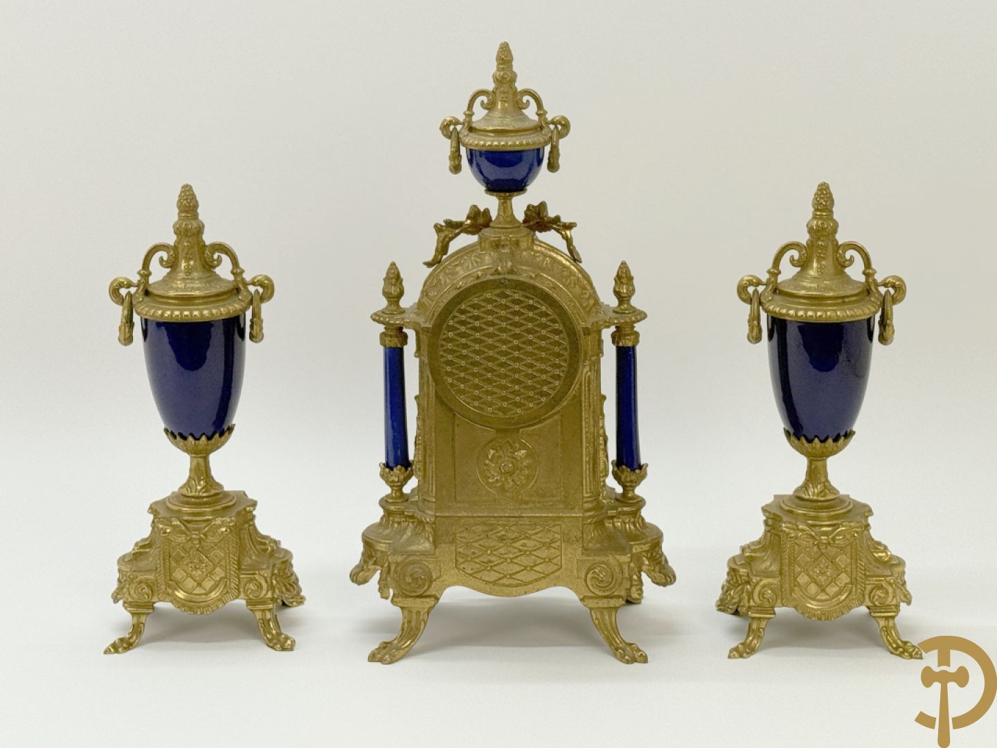 Driedelige koperen garnituur bestaande uit pendule met beschilderd romantisch tafereel en amfoor, zijdelings bezet met paar cassolettes met geanimeerde scènes, onleesbaar getekend rechts onder klok