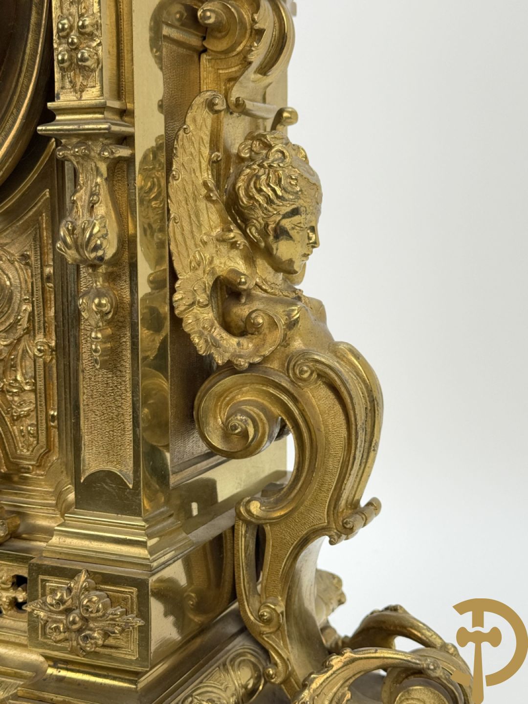 Vuurvergulde bronzen pendule, zijdelings bezet met gevleugelde dames, bovenaan met amfoor