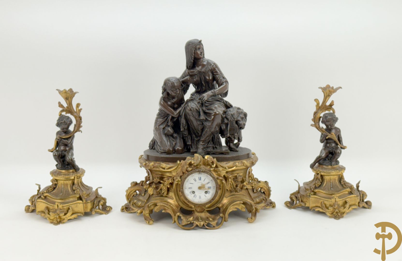 Driedelige bronzen garnituur bestaande uit middenstuk met bronzen vuurvergulde klok, Daubrée gemerkt à Nancy, bovenaan bekroond met Cleopatra met drinkbeker - getekend van Cumberworth sculpteur - geflankeerd door paar cupido