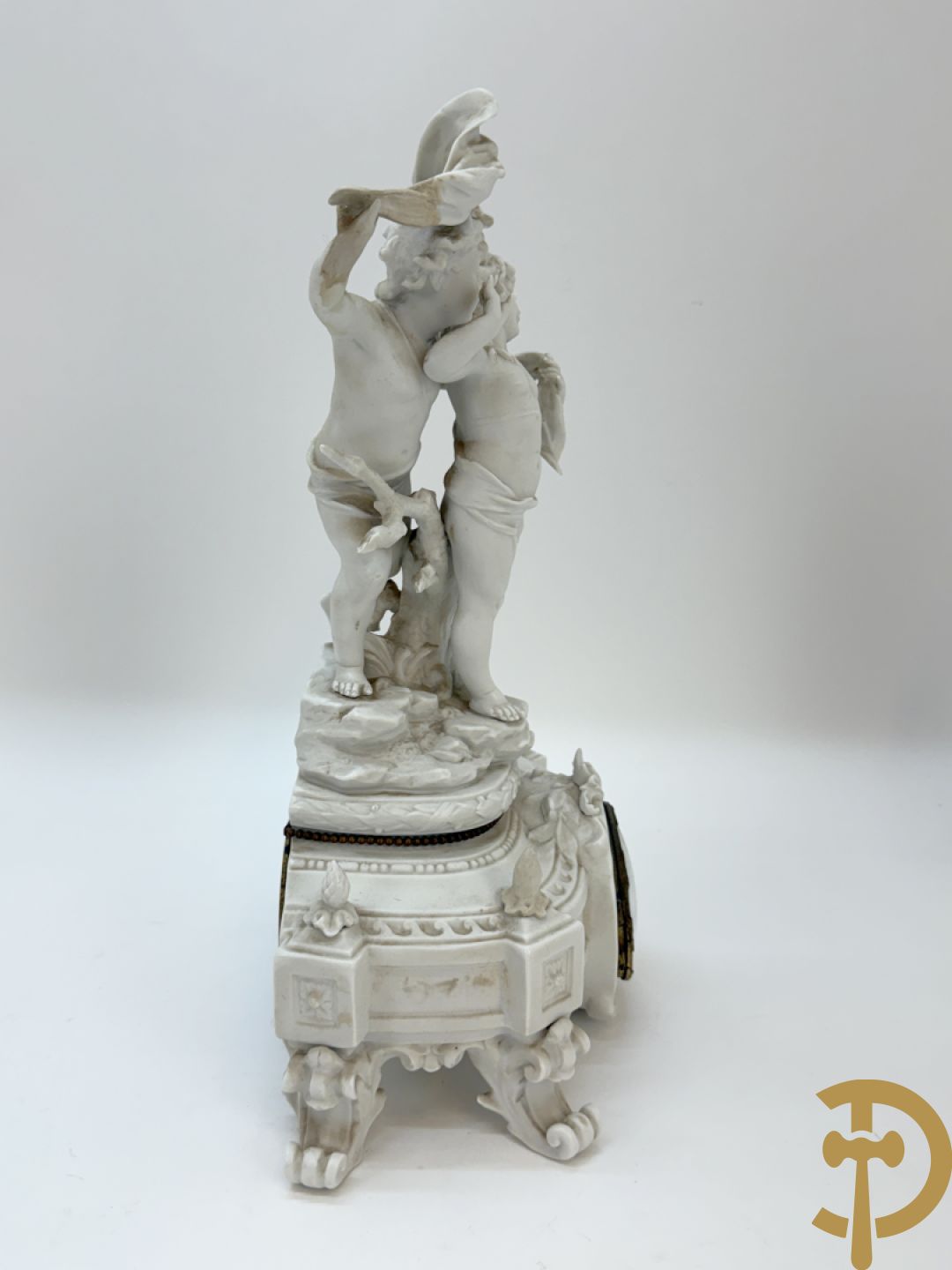 Driedelige porseleinen garnituur bestaande uit pendule bezet met lieftallig koppel, geflankeerd door paar kandelaars met cupido