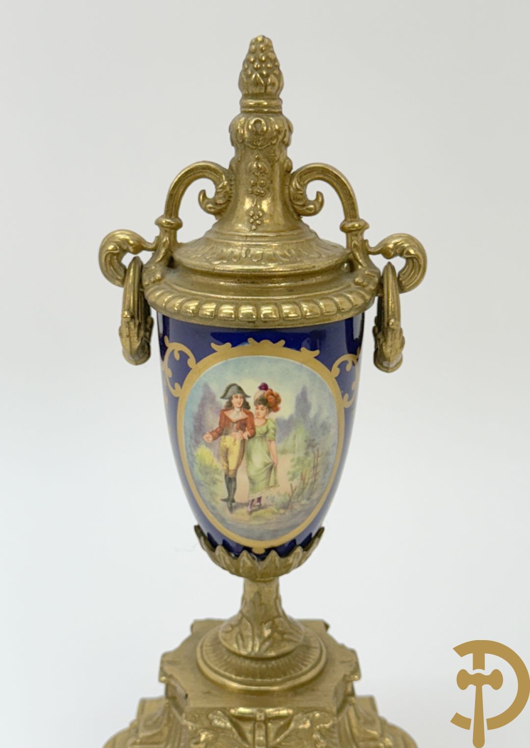 Driedelige koperen garnituur bestaande uit pendule met beschilderd romantisch tafereel en amfoor, zijdelings bezet met paar cassolettes met geanimeerde scènes, onleesbaar getekend rechts onder klok