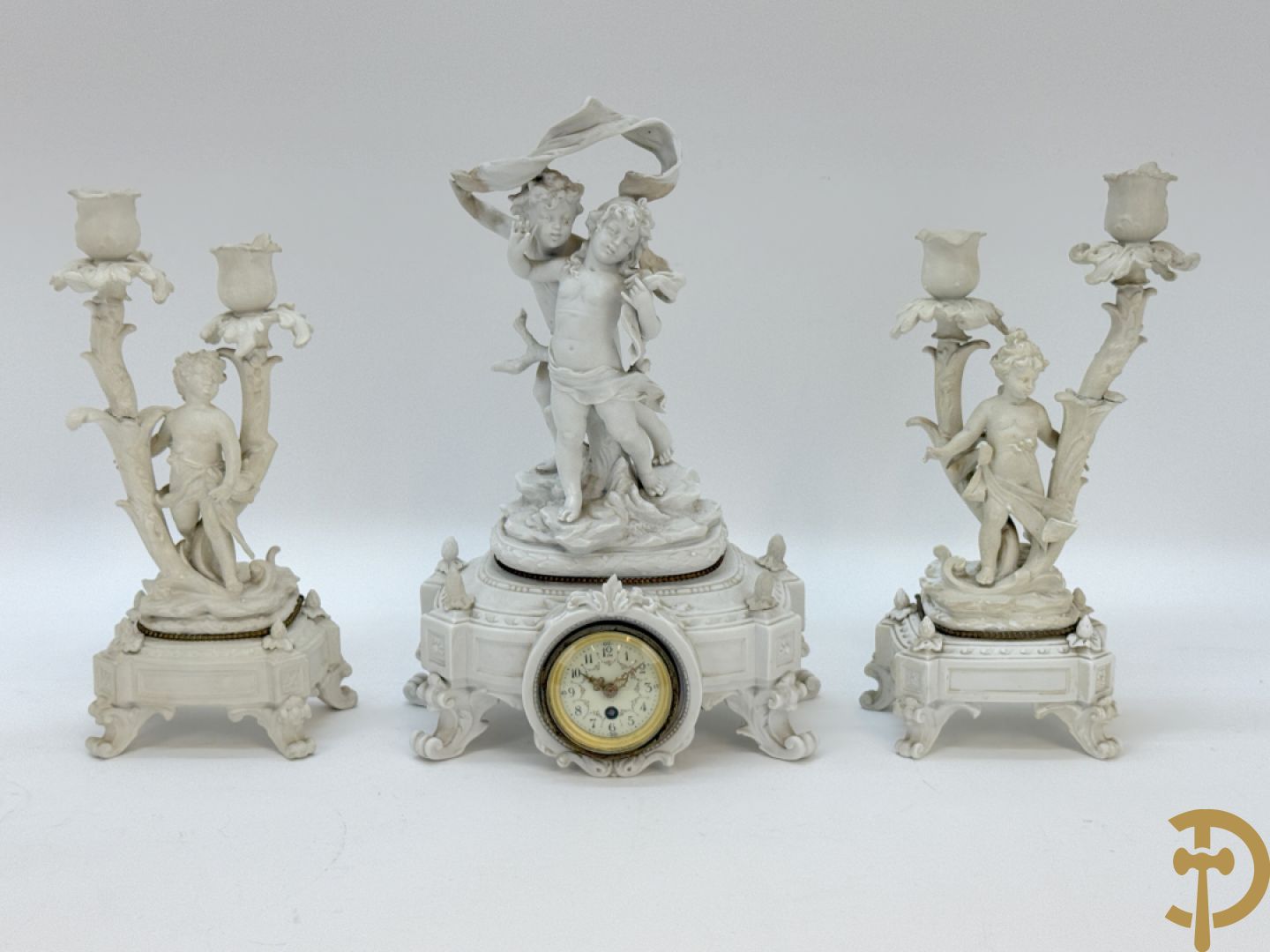 Driedelige porseleinen garnituur bestaande uit pendule bezet met lieftallig koppel, geflankeerd door paar kandelaars met cupido