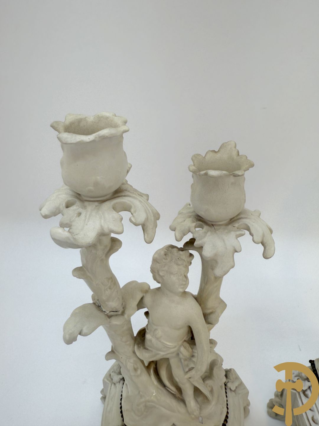 Driedelige porseleinen garnituur bestaande uit pendule bezet met lieftallig koppel, geflankeerd door paar kandelaars met cupido