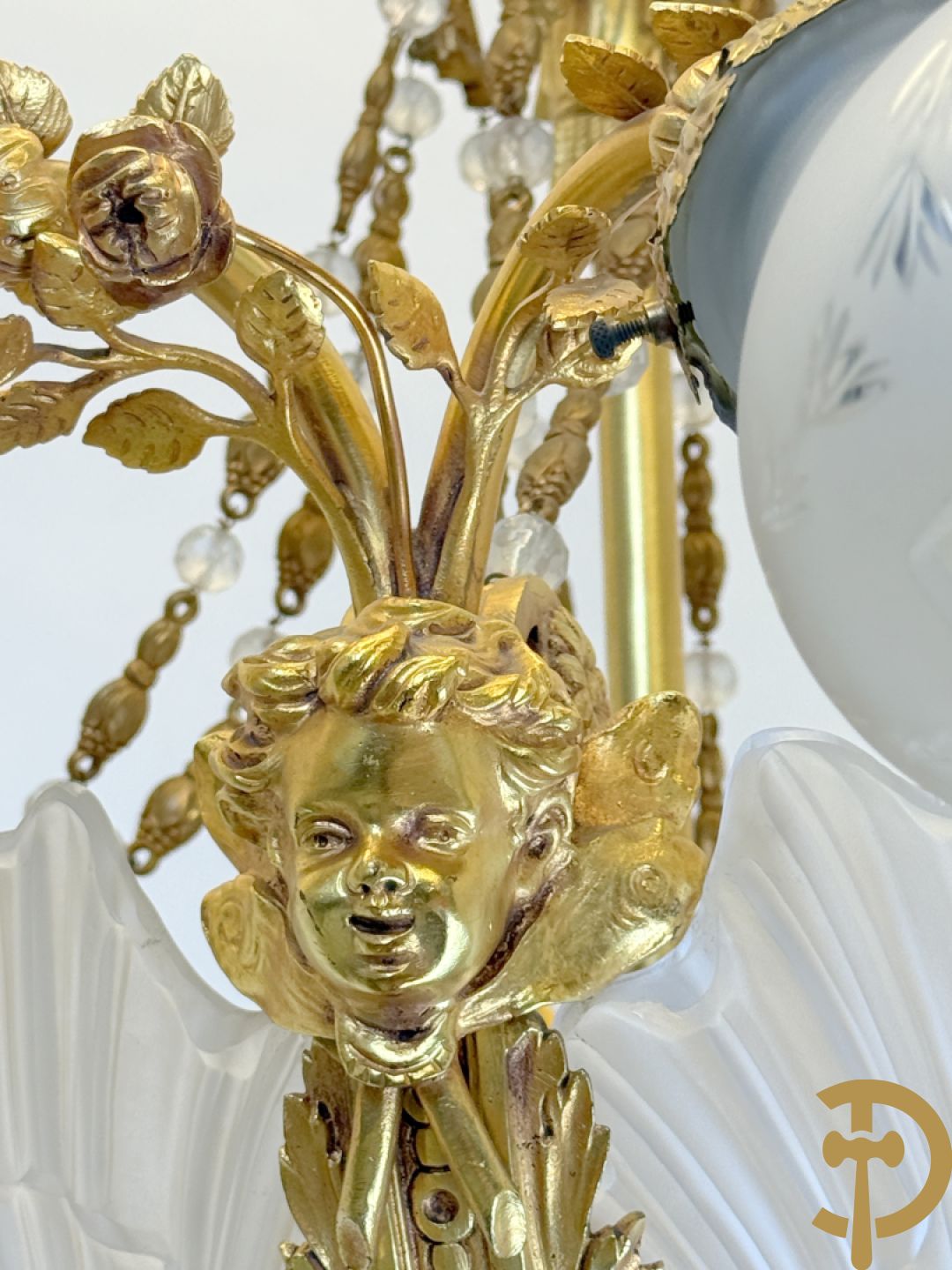 Bronzen vuurvergulde luchter met 4 paar lichtpunten bezet met bladranken, onderaan met glazen schelpen en armen bezet met cupidohoofden