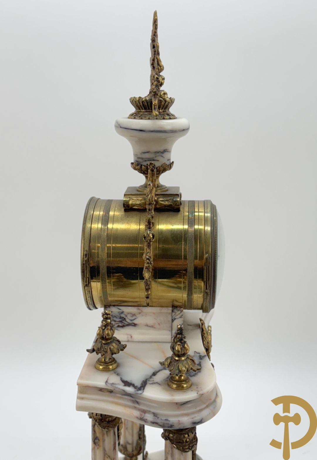 Driedelige wit marmeren garnituur bestaande uit vierzuilenpendule met bloemen en troffee geflankeerd door paar cassolettes met ramskoppen bezet