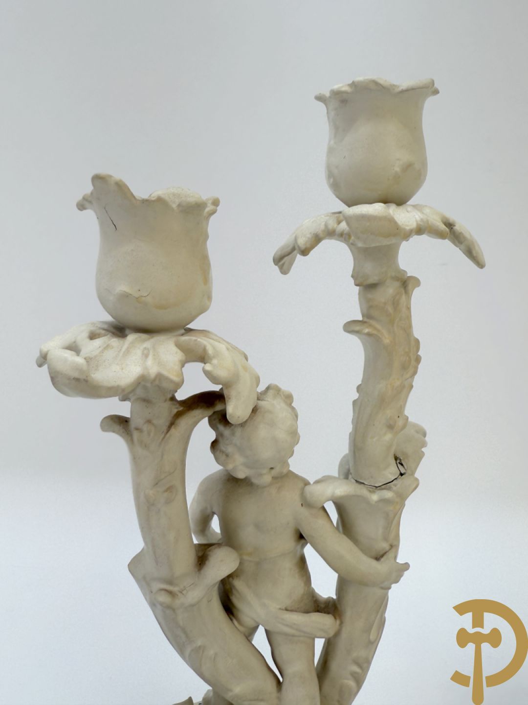 Driedelige porseleinen garnituur bestaande uit pendule bezet met lieftallig koppel, geflankeerd door paar kandelaars met cupido