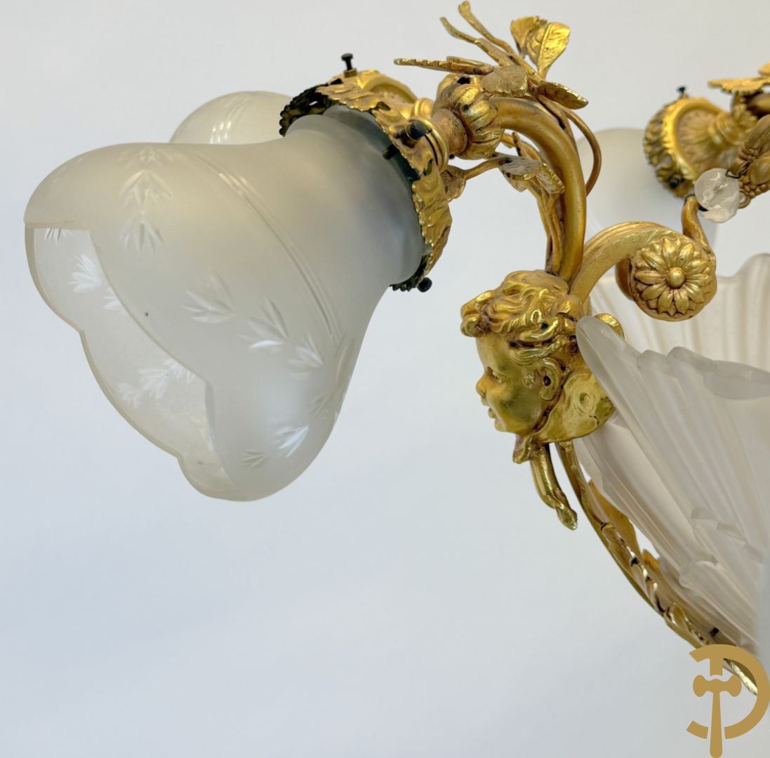 Bronzen vuurvergulde luchter met 4 paar lichtpunten bezet met bladranken, onderaan met glazen schelpen en armen bezet met cupidohoofden
