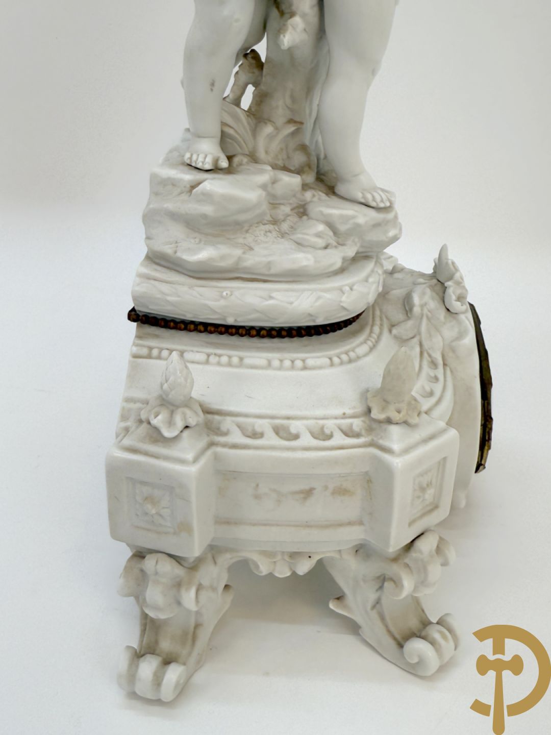 Driedelige porseleinen garnituur bestaande uit pendule bezet met lieftallig koppel, geflankeerd door paar kandelaars met cupido