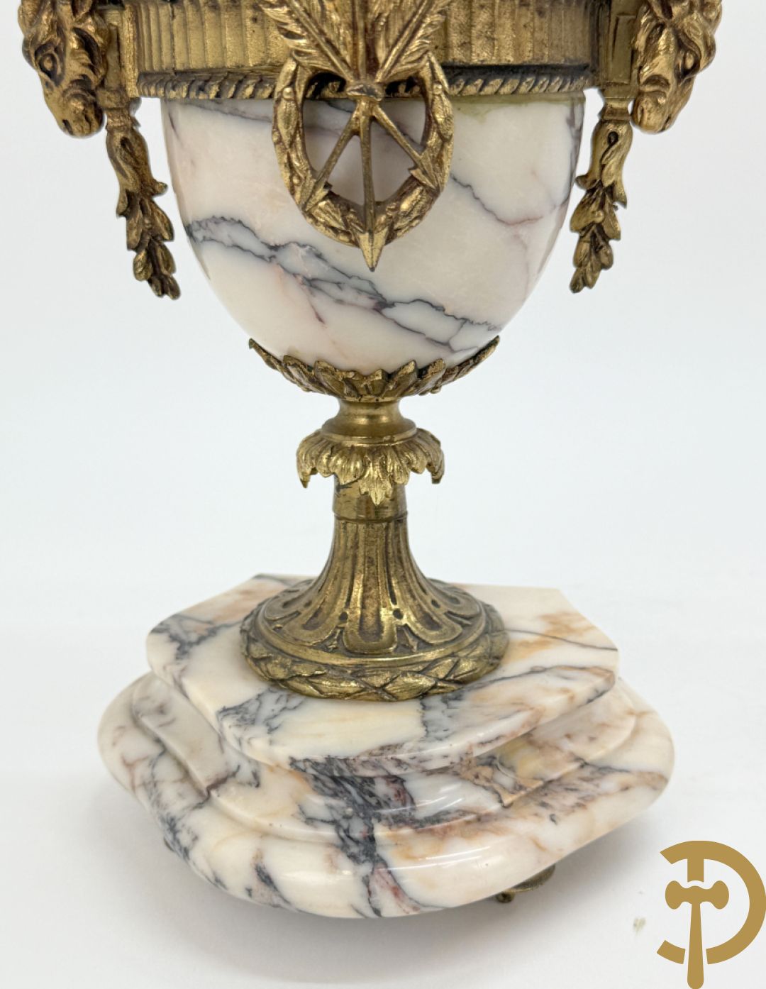 Driedelige wit marmeren garnituur bestaande uit vierzuilenpendule met bloemen en troffee geflankeerd door paar cassolettes met ramskoppen bezet