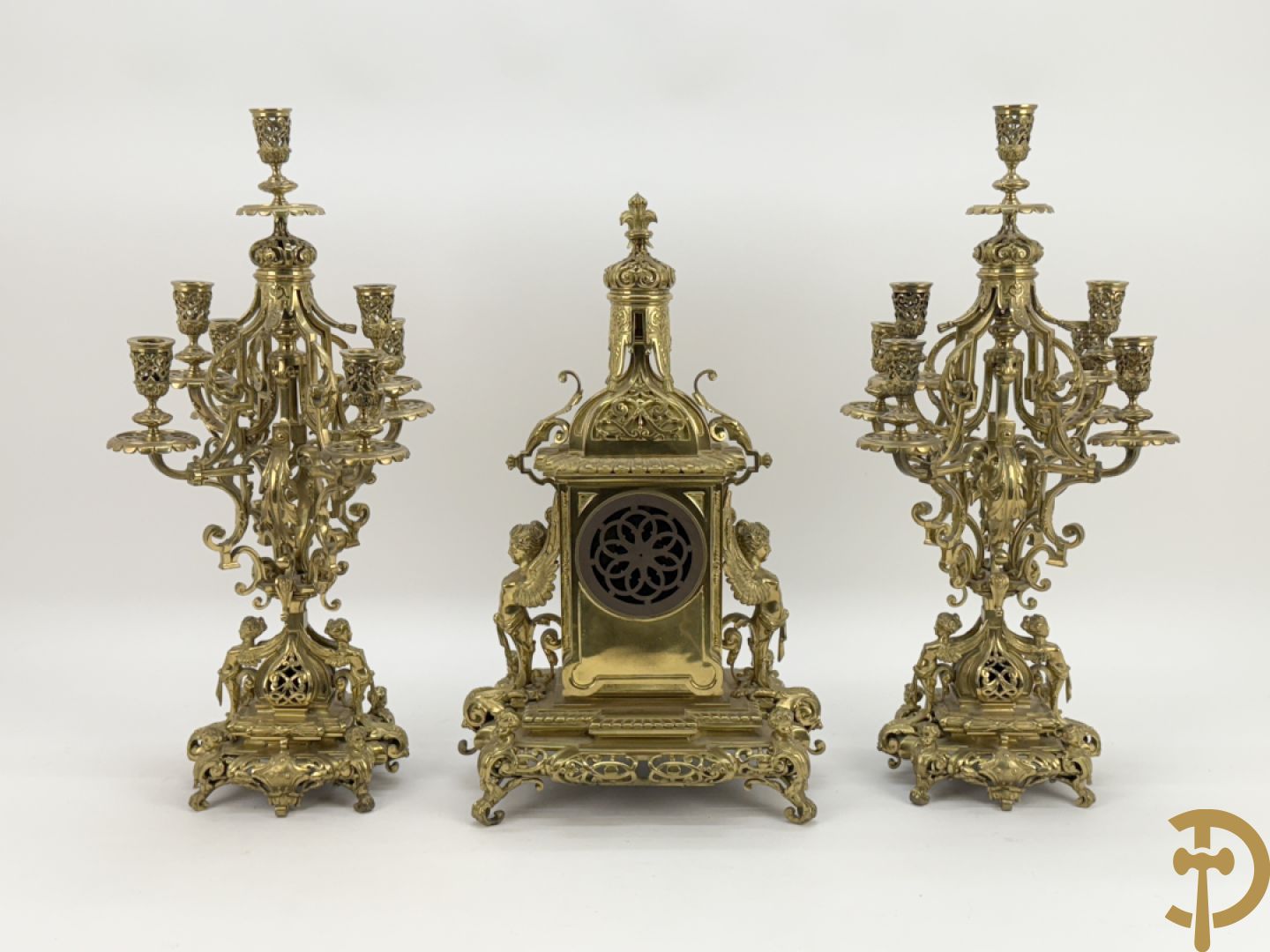 Driedelige bronzen vergulde garntiuur bestaande uit klok met medusahoofden en sfinxen, geflankeerd door paar zevenarmige kandelaars met accanthusranken en sfinxen